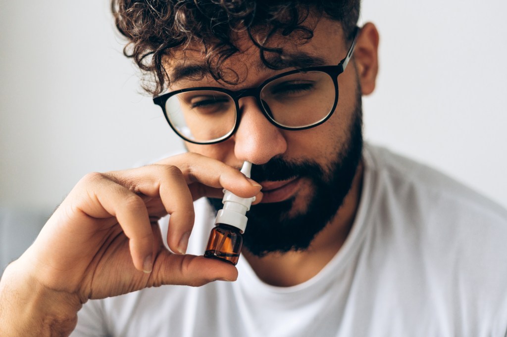 Close-up of sick middle eastern man with glasses using nasal spray.