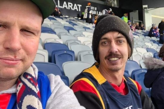 Two men are sitting and watching a football match in a stadium. 