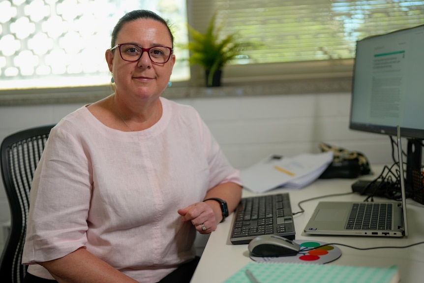 A woman sits at a table and smiles at the camera. 