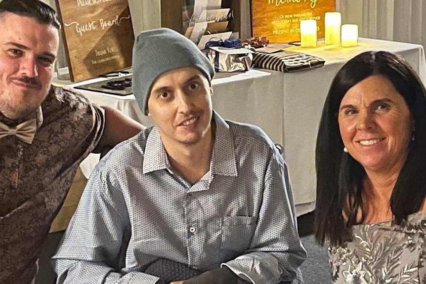 A man with a bow tie, a man wearing a beanie hat and a woman sit together. 