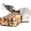 This photo shows a granola bar with its wrapper open and partially retracted. It lies on a white surface and against a white background.