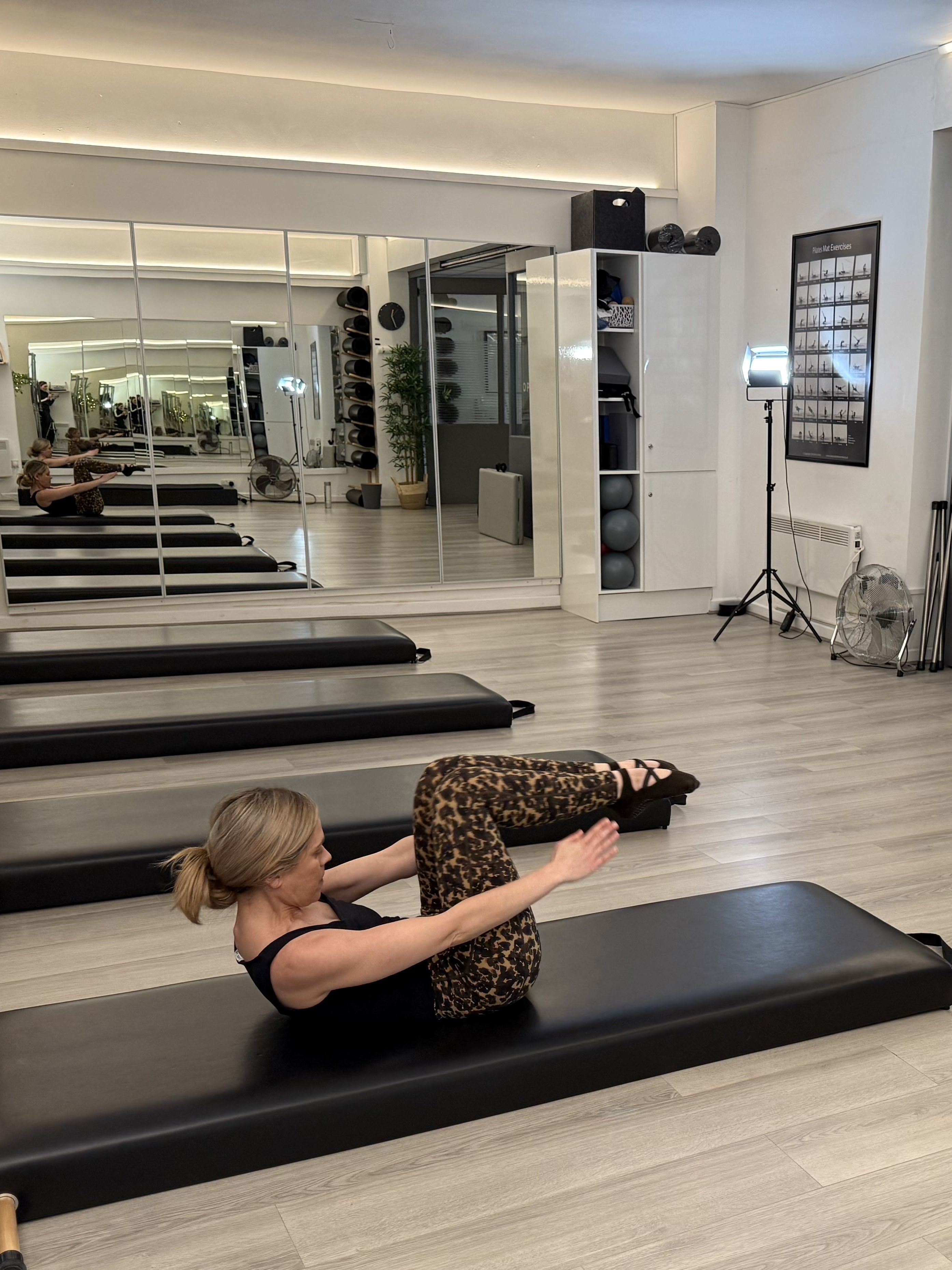 A woman demonstrates a Pilates move in a studio setting