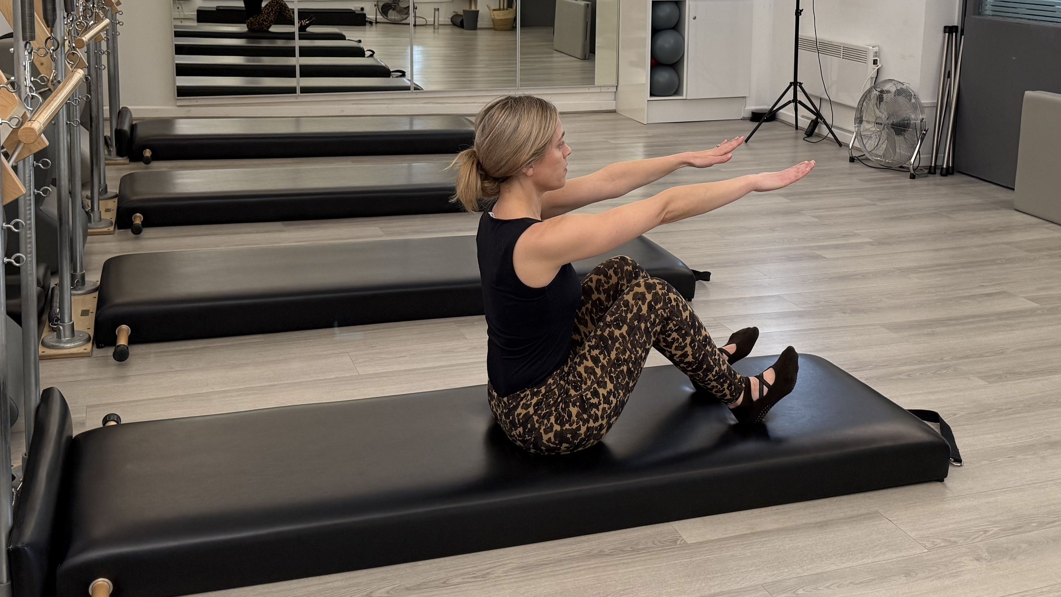 A woman demonstrates a Pilates move in a studio setting