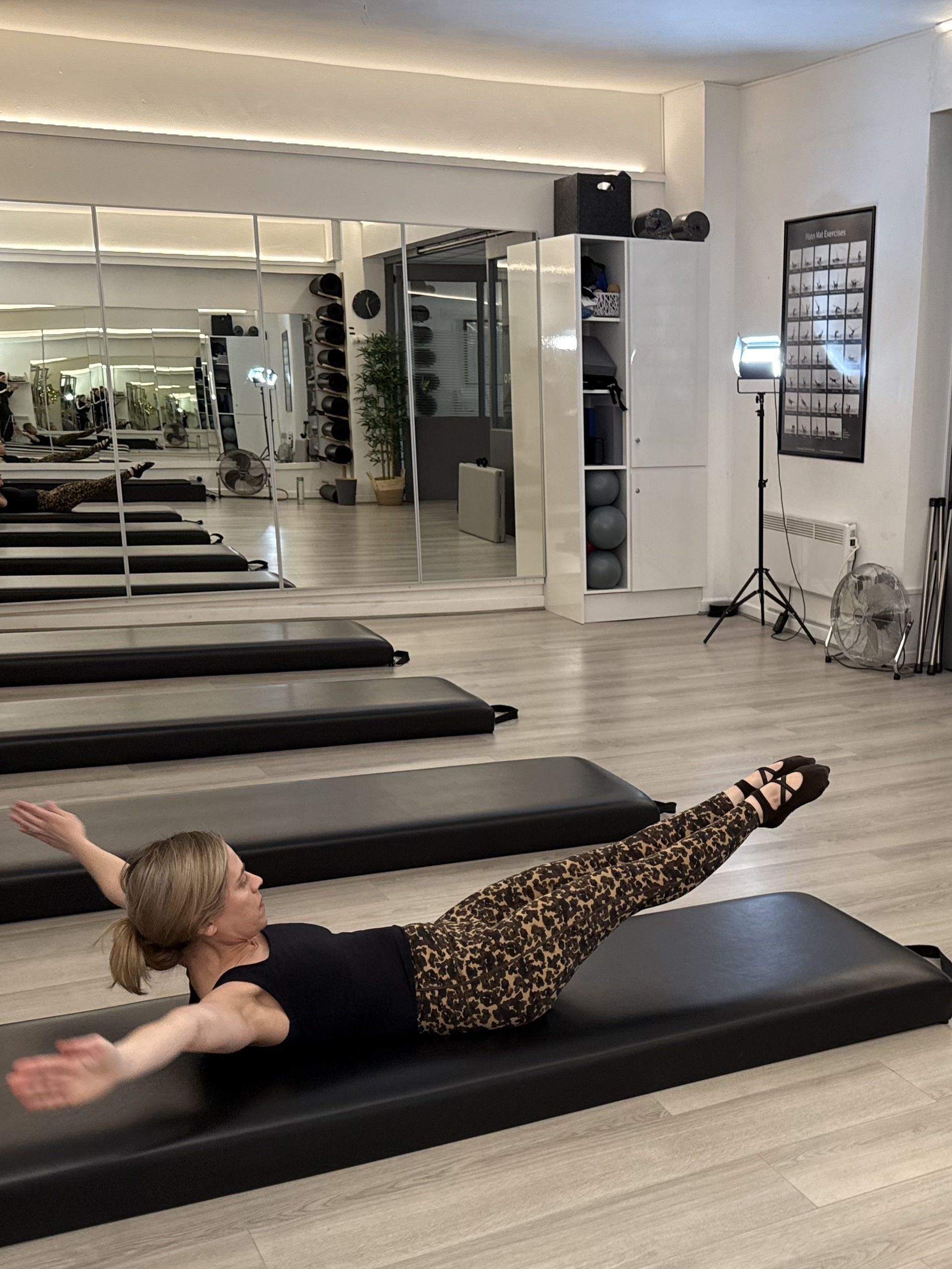 A woman demonstrates a Pilates move in a studio setting