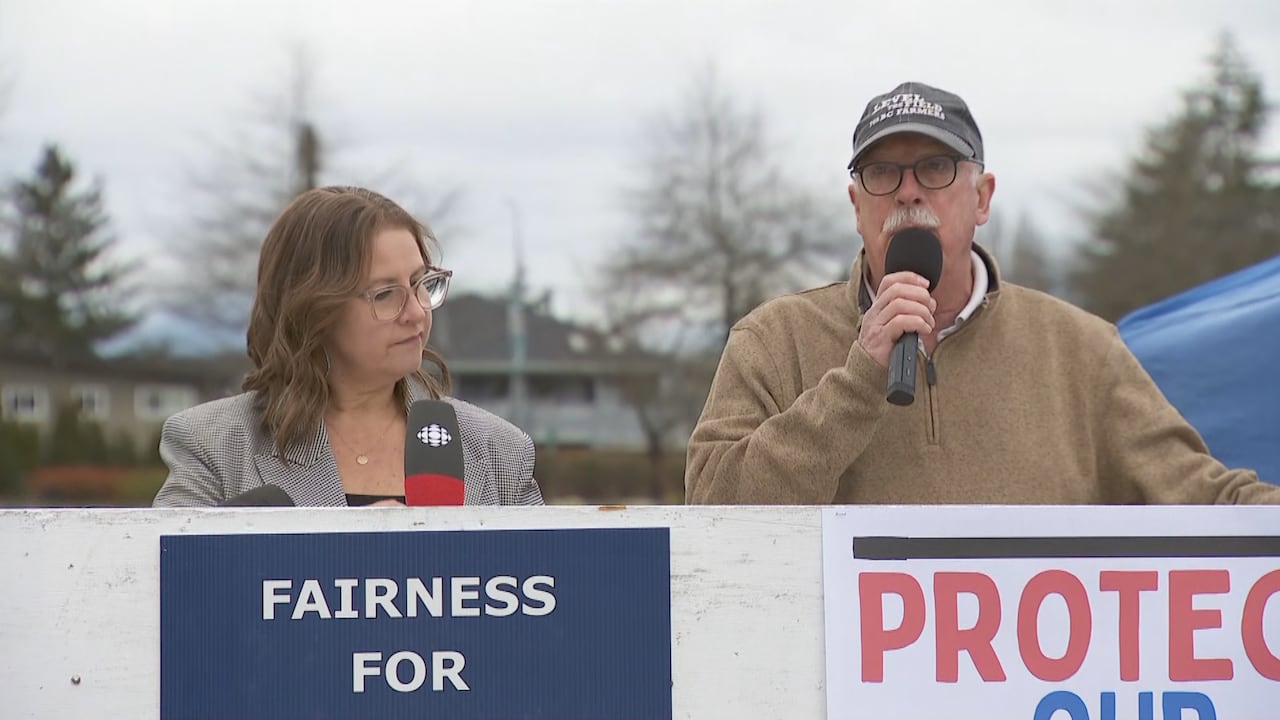 A man speaks into a microphone next to a woman standing behind signs at a protest.