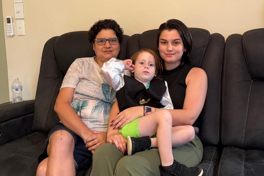 Belinda Menzies (left) sits on the sofa with Maddie Menzies, 24, and Elliott.