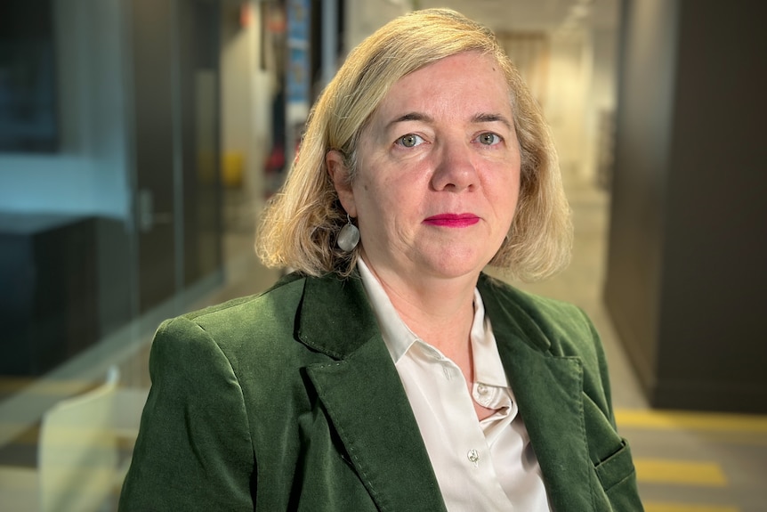 Profile photo of a woman with short white hair in a green blazer and white shirt and red lipstick.