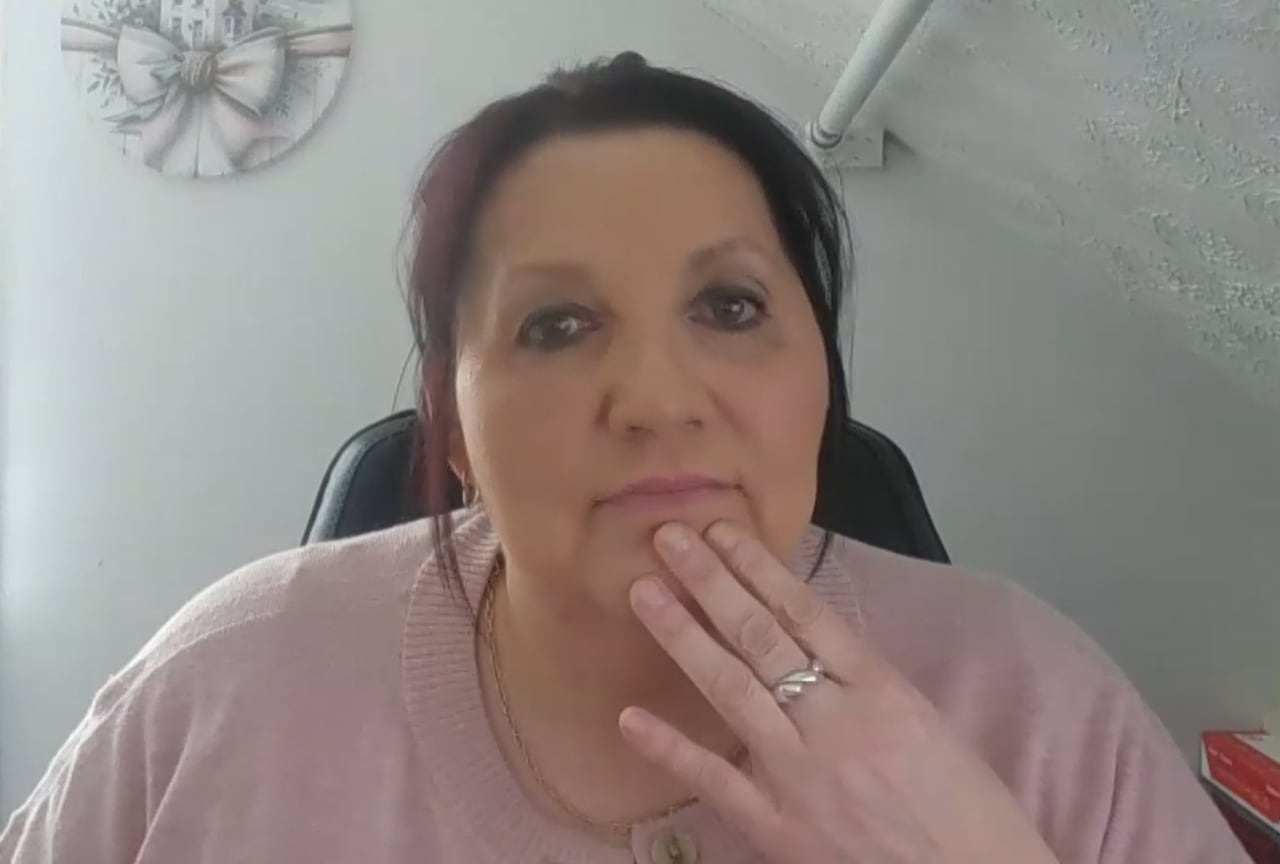 Yvette Jarvis sits wearing a pink top and looks at the camera with her hand on her chin.