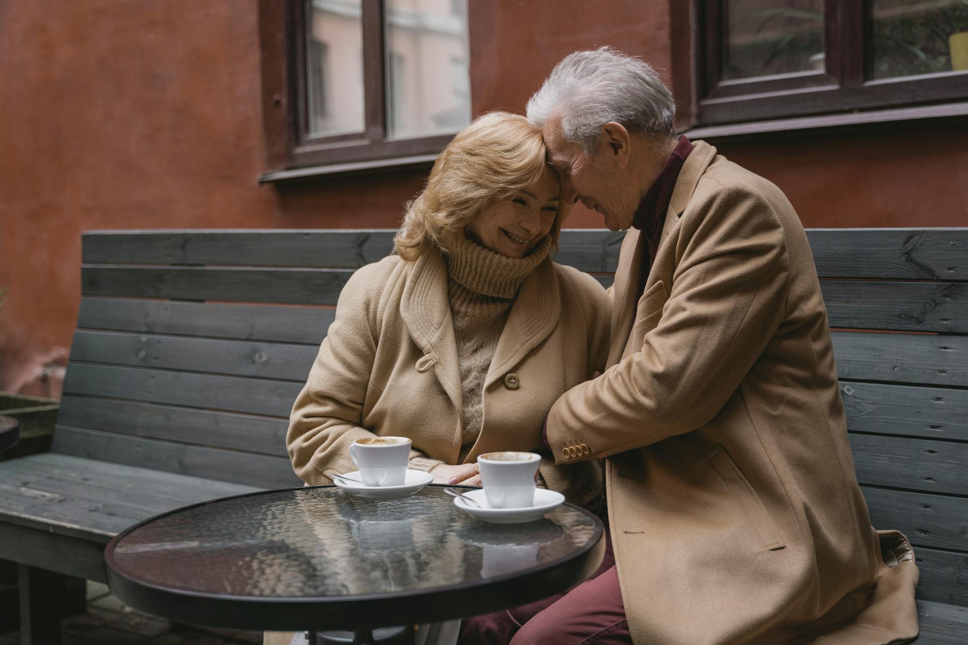 Lovely old couple sharing coffee on a cozy outdoor bench, showing warmth and love.