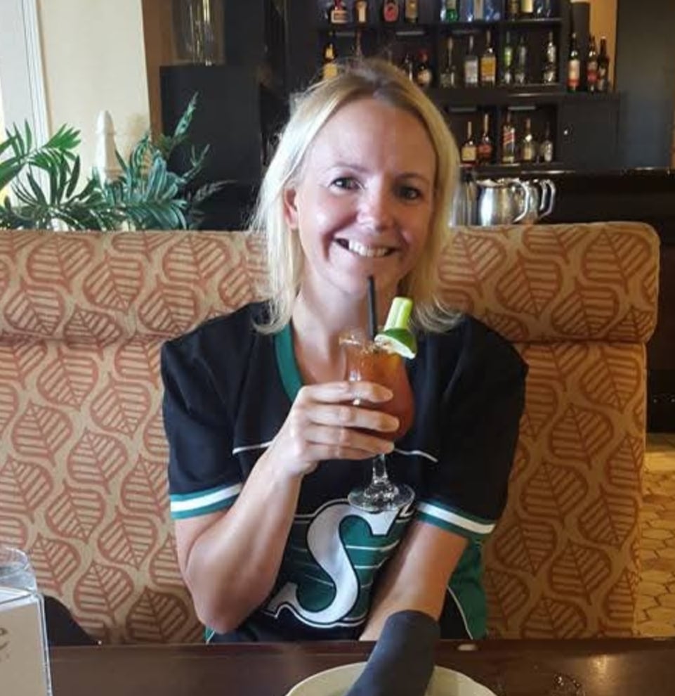 A woman in a black and green jersey sits at a restaurant booth holding a drink.