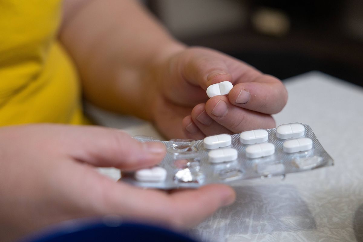 Woman taking medicine for headache while drinking tea in kitchen.