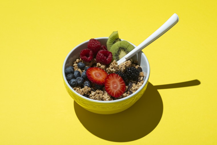 Bowl with muesli, chocolate and fruit on a yellow background